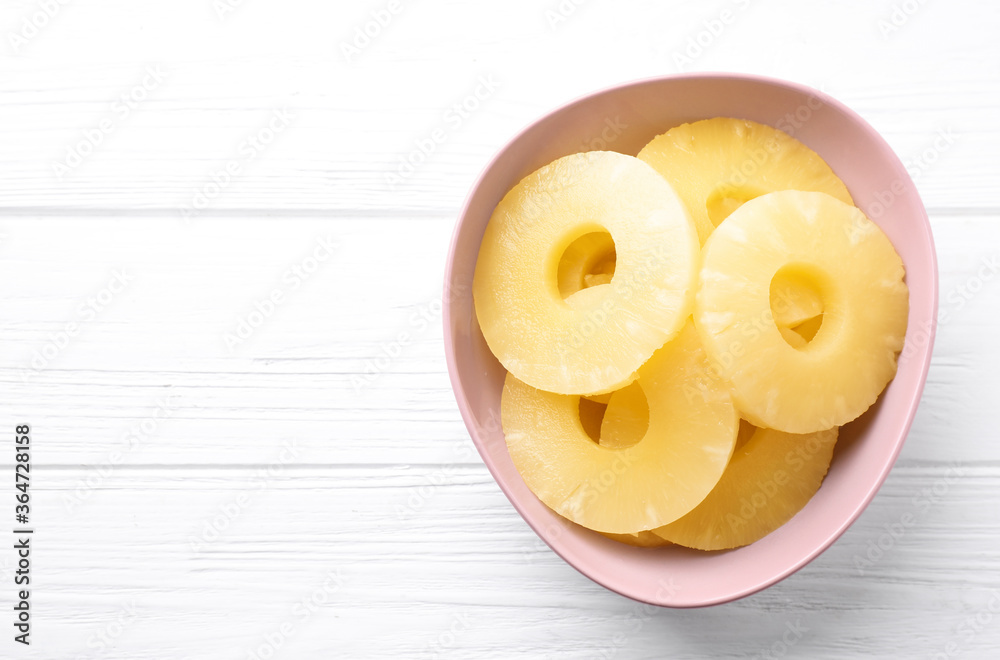 Delicious canned pineapple rings in bowl on white wooden table, top view. Space for text Delicious canned pineapple rings in bowl on white wooden table, top view. Space for text