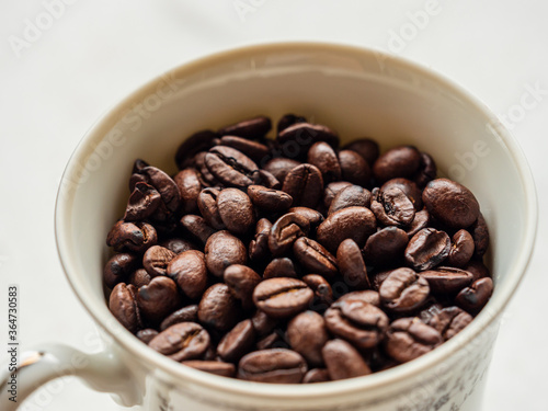 High angle view of roasted coffee beans in a white porcelain cup on a white background