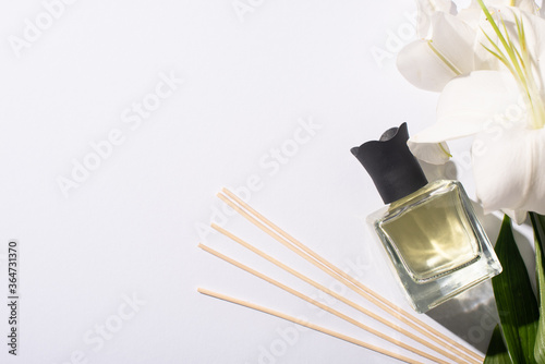 top view of aroma sticks with perfume in bottle near lilies on white background