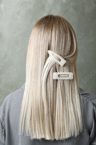 Young woman with beautiful hair clips on grey background, back view