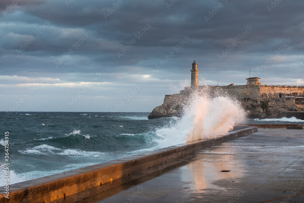 Big waves on Malecon streets during sunrise with storm clouds in background. Havana, Cuba