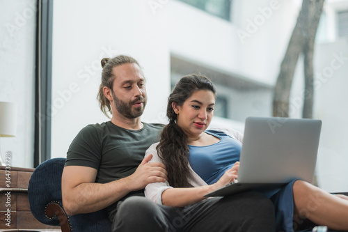 Beard man and his pregnant wife watching movie on laptop feeling happy while sitting on sofa in the home. Family concept.