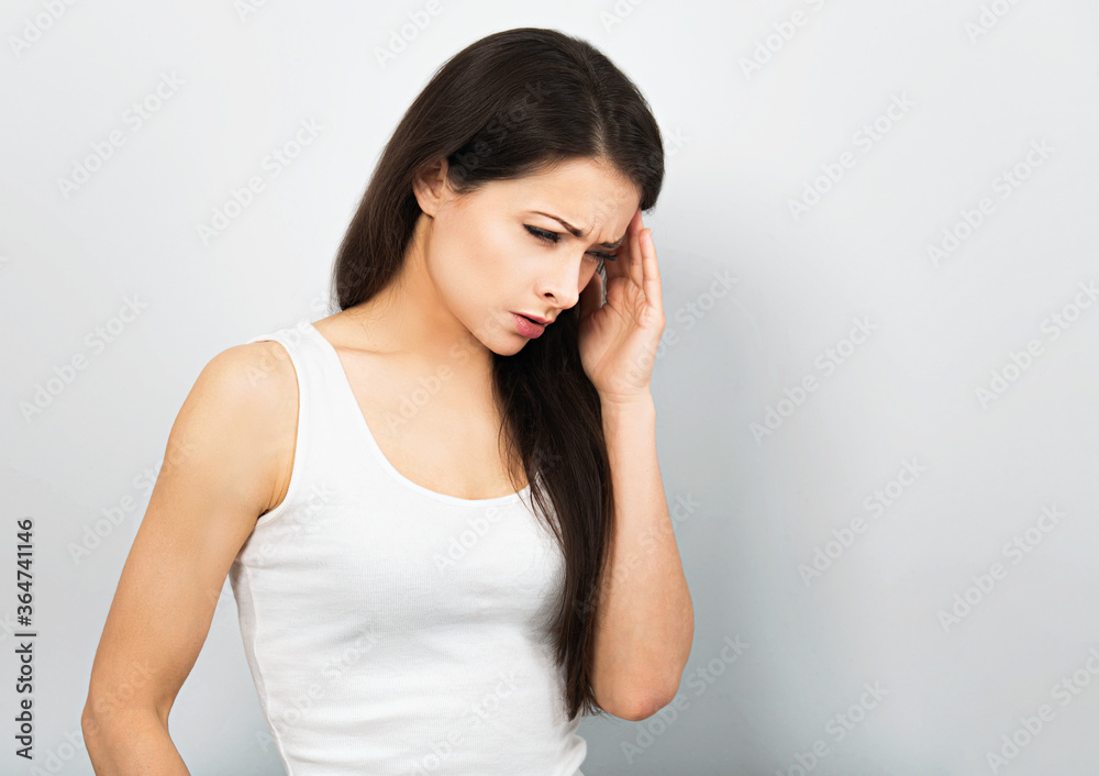 Beautiful angry unhappy thinking woman holding the hand with headache and raised eyebrow on blue background. Closeup portrait Beautiful angry unhappy thinking woman holding the hand with headache and raised eyebrow on blue background. Closeup portrait