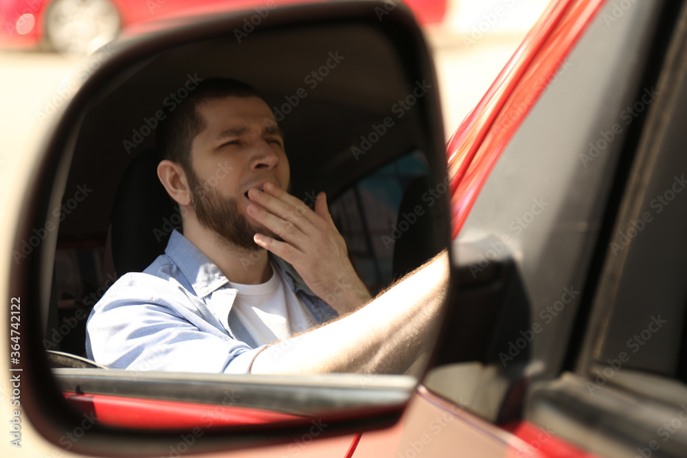 Tired man yawning in his auto, view through car side mirror