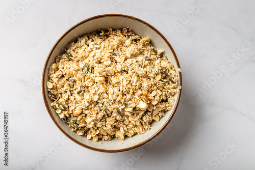 Ingredients for healthy homemade granola with Gluten Free Rolled oats or porridge oats, variety of chopped nuts and seeds, and maple syrup. Preparation for cooking at home, all mixed in bowl.