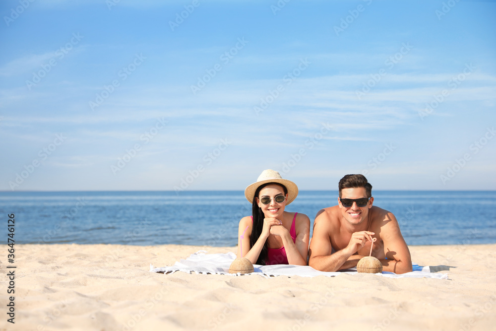 Happy couple with cocktails on sunny beach at resort. Space for text