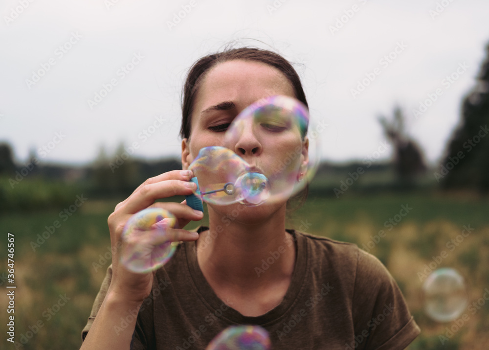 The girl blows soap bubbles. A young woman sits in nature and blows soap balls. The person in front. The girl blows soap bubbles. A young woman sits in nature and blows soap balls. The person in front.