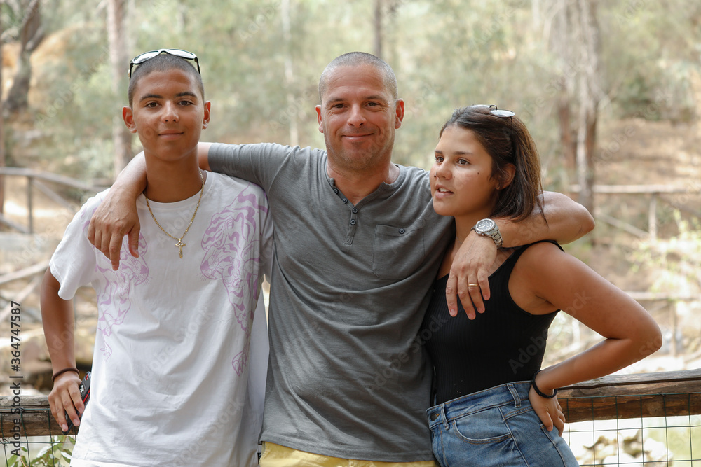 Obraz premium Padre Europeo con i due figli Italo-Brasiliani si abbracciano felici in mezzo a un parco