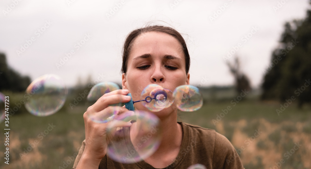 The girl blows soap bubbles. A young woman sits in nature and blows soap balls. The person in front. The girl blows soap bubbles. A young woman sits in nature and blows soap balls. The person in front.