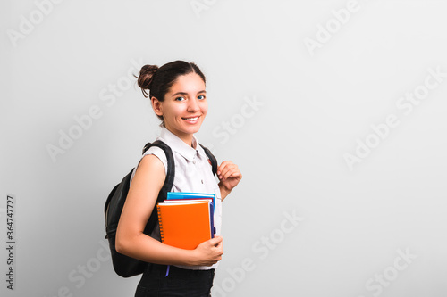 attractive female student with dimples in cheeks smiling holding notebooks in one hand and backpack on shoulders with cute face expression