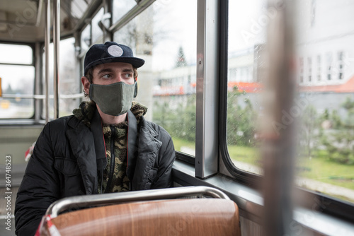 Male wearing face mask inside public transport watches at the window with rainy weather 