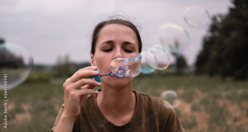 The girl blows soap bubbles. A young woman sits in nature and blows soap balls. The person in front.