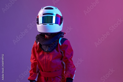 Foto Cool boy child racer in helmet, racing suit, standing in neon light