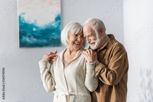 cheerful senior man touching shoulders of happy wife