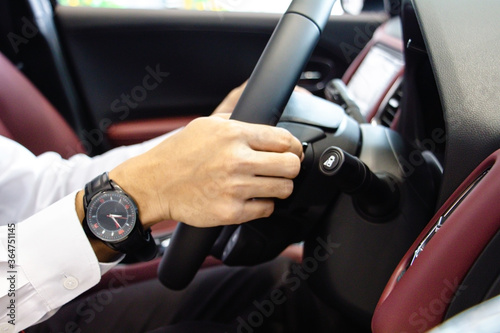 Close-up A businessman Hands put a watch Holding Steering Wheel with red console. Driving car concept. © setthawuth