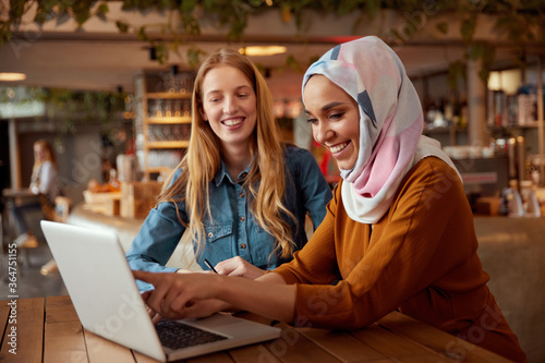 Business. Colleagues Meeting In Cafe. Diversity Ethnic Women. Smiling Girl In Hijab Working On Laptop, Blonde Looking At Screen. photo