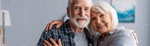 horizontal image of happy senior couple smiling and embracing while looking at camera