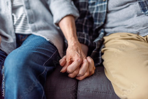 cropped view of senior couple sitting on sofa and holding hands