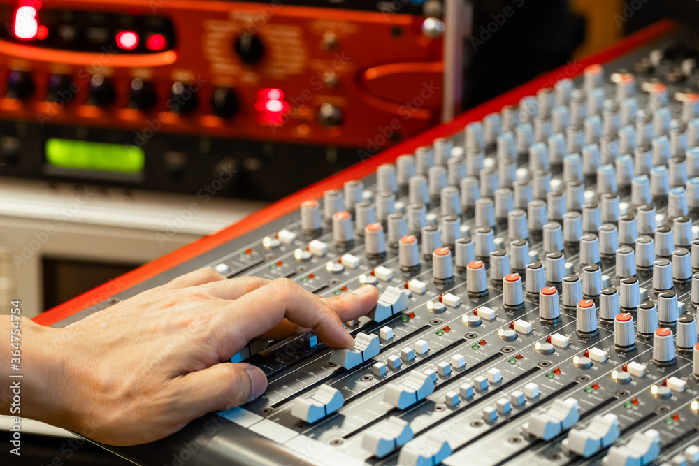 sound engineer hand adjusting audio level on mixing console in broadcasting studio