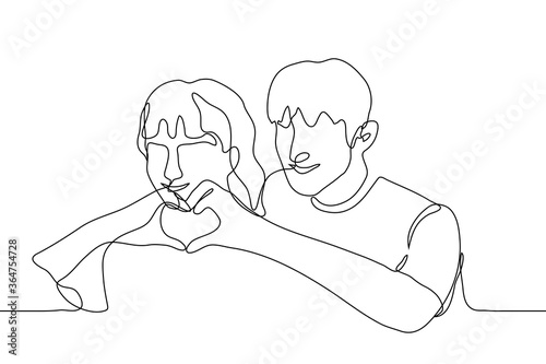 Foto pair of young people (guy and girl) stand nearby and folded a silhouette of the heart with their fingers