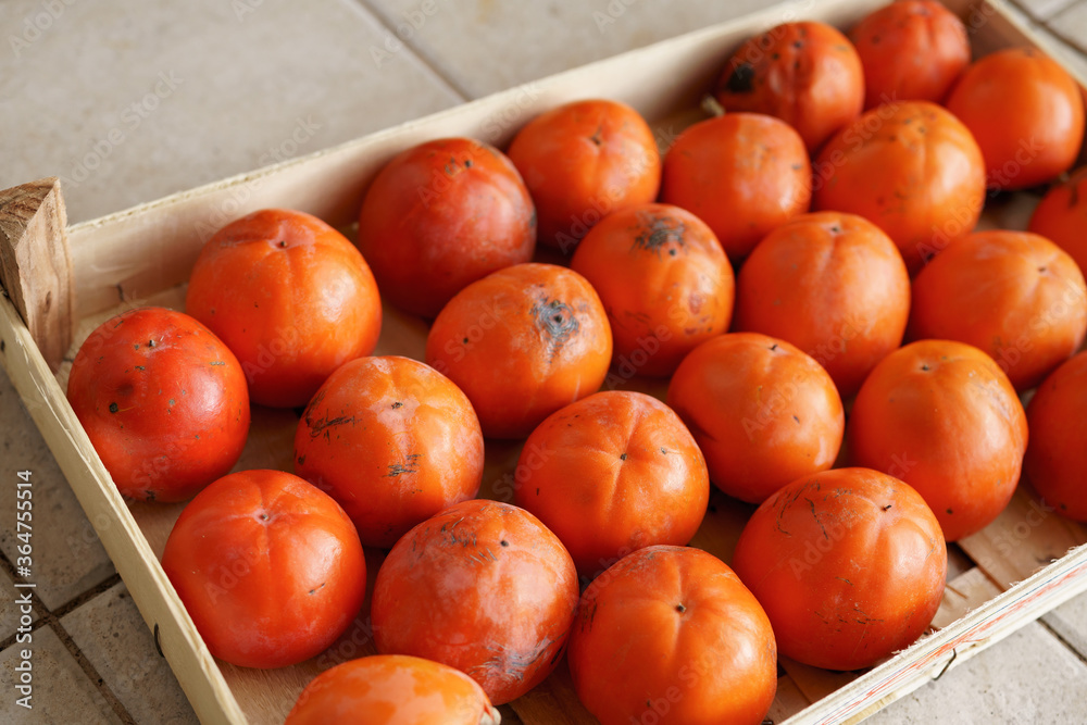 Ripe orange persimmons in a drawer. The texture of the background is from persimmon fruit.