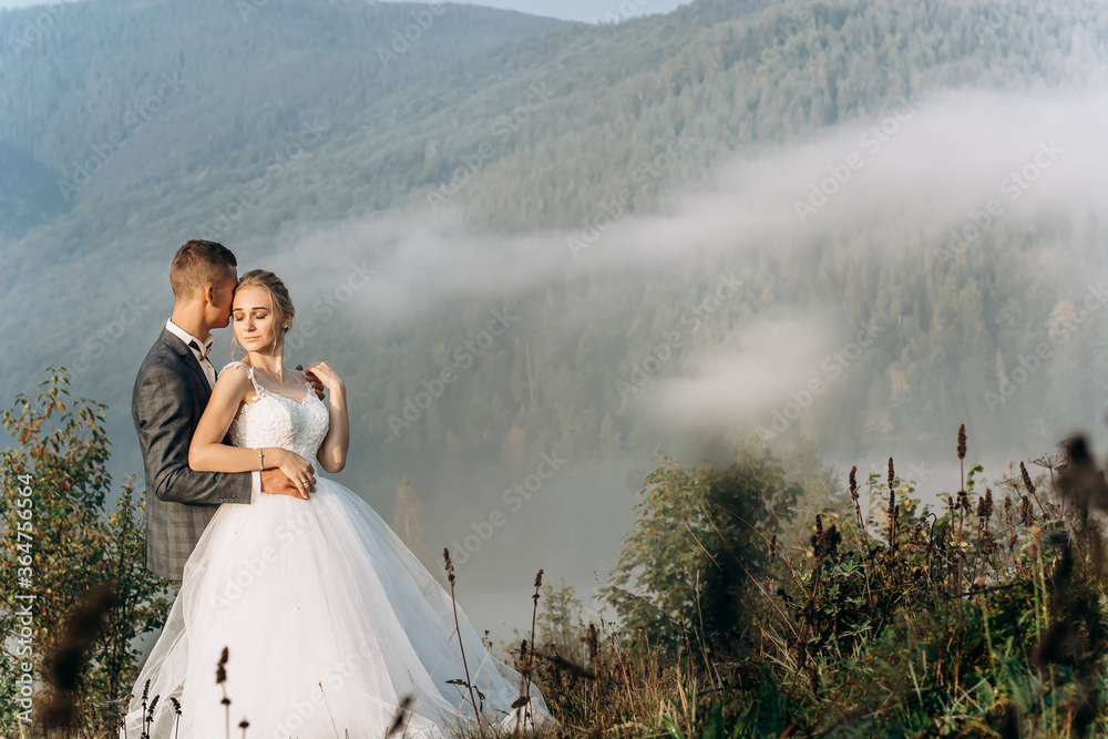 Beautiful wedding couple walk and hold hands during morning trip in mountains.