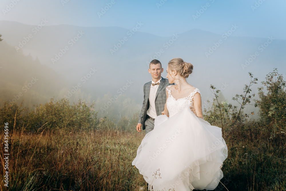 Beautiful wedding couple walk and hold hands during morning trip in mountains.