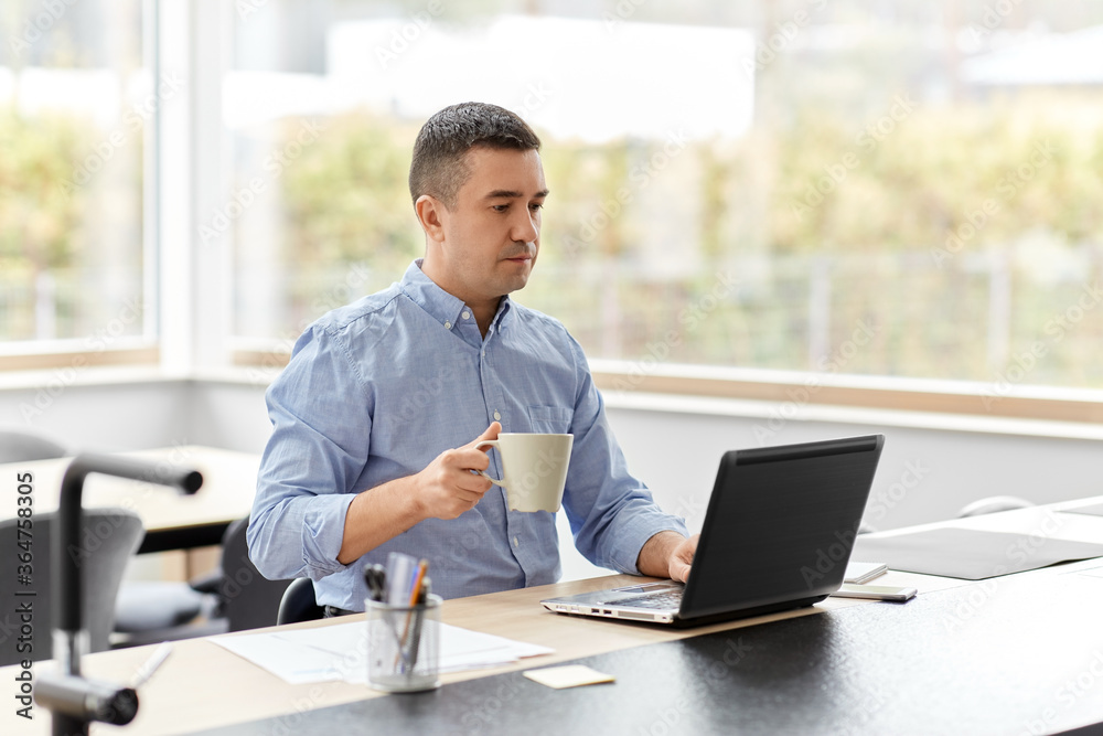 remote job, business and people concept - middle-aged man with laptop computer working at home office and drinking coffee remote job, business and people concept - middle-aged man with laptop computer working at home office and drinking coffee