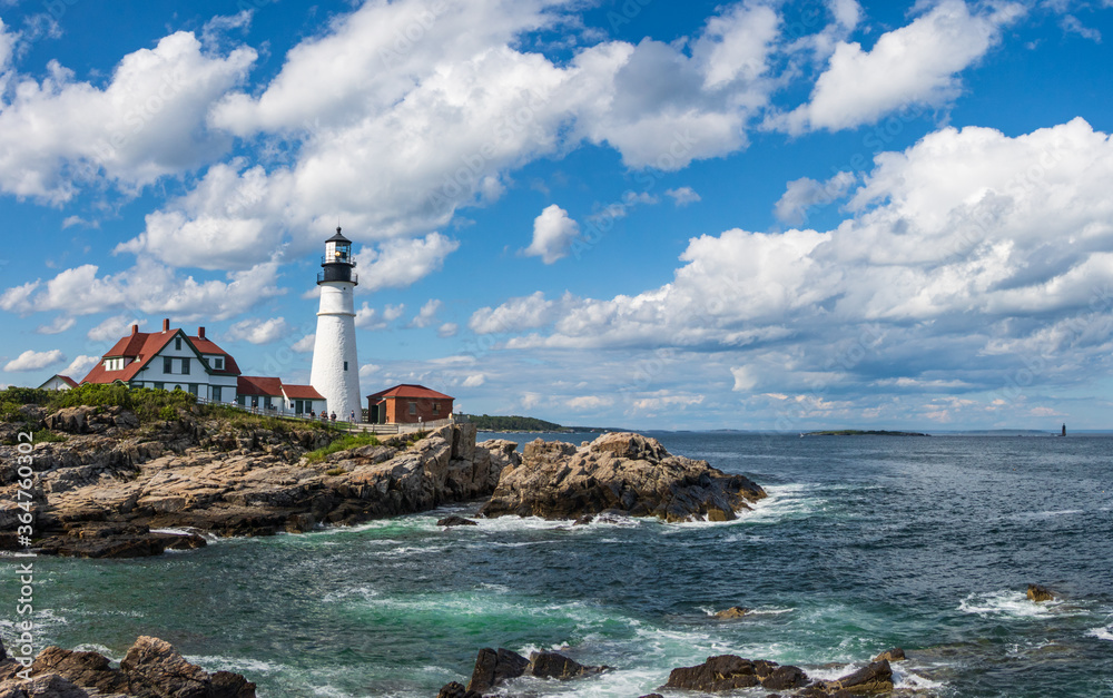 Light house on a rocky seacoast with blue sky and white clouds