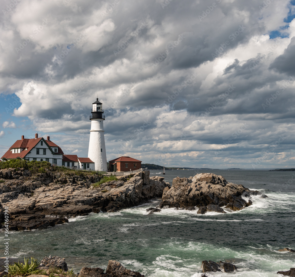 Light house on a rocky seacoast with blue sky and white clouds