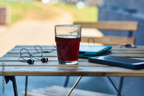 Wooden table with glass of black strong coffee and mobile headphones, smartphone and e-book. Work and study in cafe.
