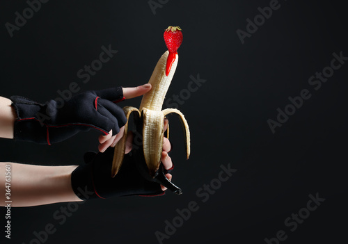 Hands holding a painted black banana on a black background. Concept for sex shops, adult toys © Yevheniia
