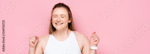 Foto horizontal image of excited overweight girl showing winner gesture on pink