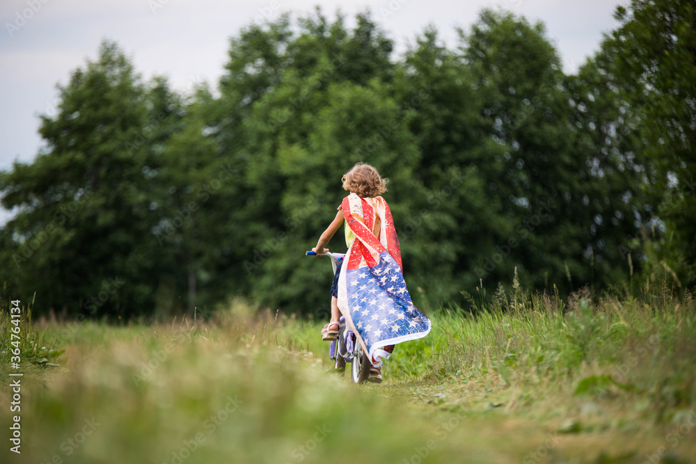 Symbol of celebration 4 fourth of july. Young Girl riding bicycle with american flag in hand Symbol of celebration 4 fourth of july. Young Girl riding bicycle with american flag in hand