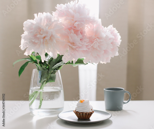 Peony flowers, coffee and cake. Romantic composition. Beautiful pink peonies in a vase at home interior. 