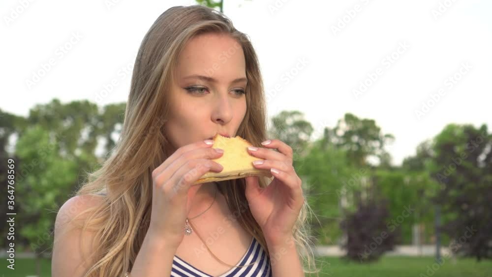 Young beautiful woman eating a fast food sandwich on the street Young beautiful woman eating a fast food sandwich on the street
