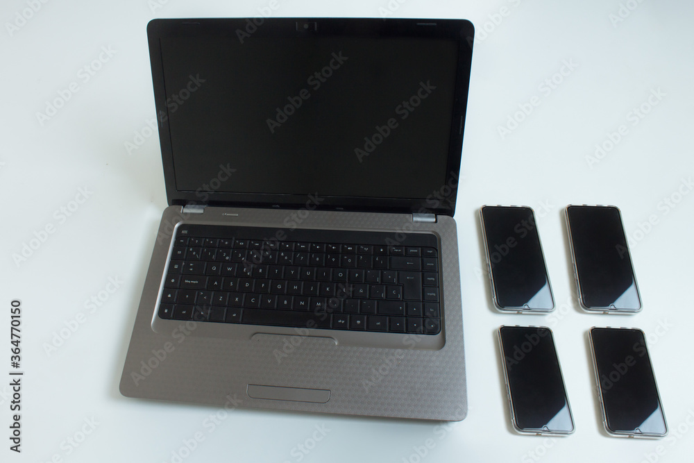 An open laptop computer with four mobile phones on one side on a white background. An open laptop computer with four mobile phones on one side on a white background.