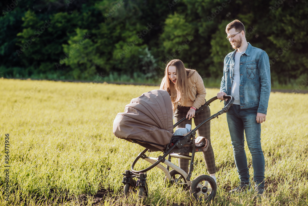 Happy parents with love and tenderness look at their child who is lying in a stroller Happy parents with love and tenderness look at their child who is lying in a stroller