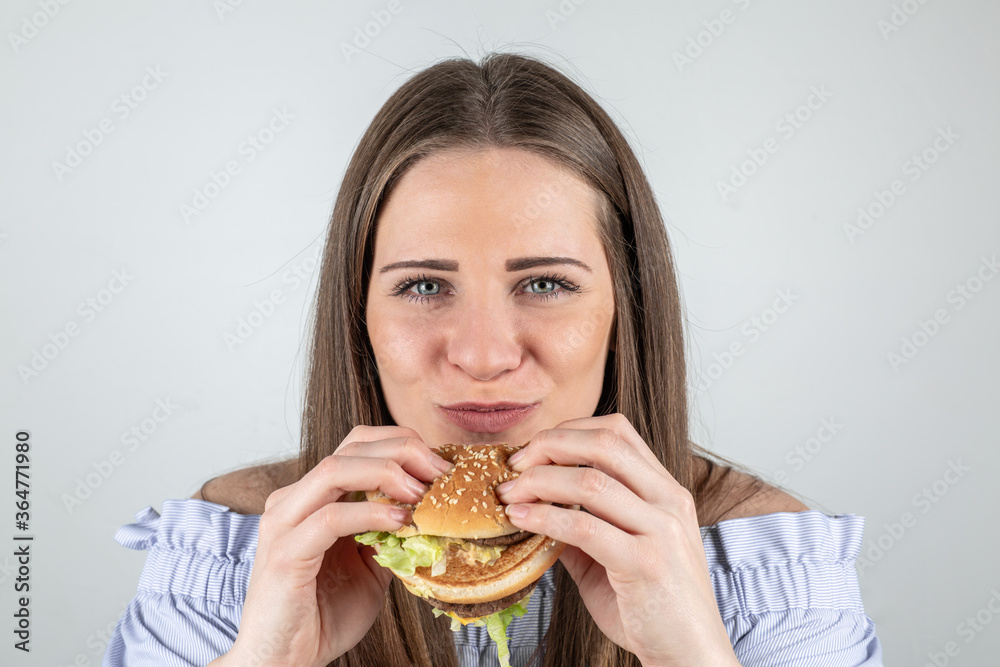 Portrait of a beautiful young woman eating a burger, isolated on white background Portrait of a beautiful young woman eating a burger, isolated on white background
