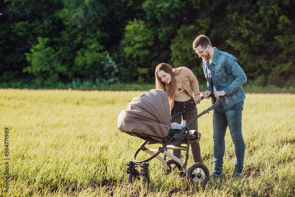Happy parents with love and tenderness look at their child who is lying in a stroller Happy parents with love and tenderness look at their child who is lying in a stroller