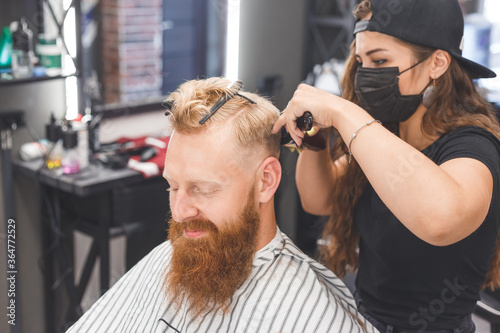 Woman barber making haircut to redhaired man with beard in barbershop