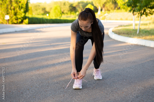 Woman athlete runner tie her shoelaces in the summer before run.