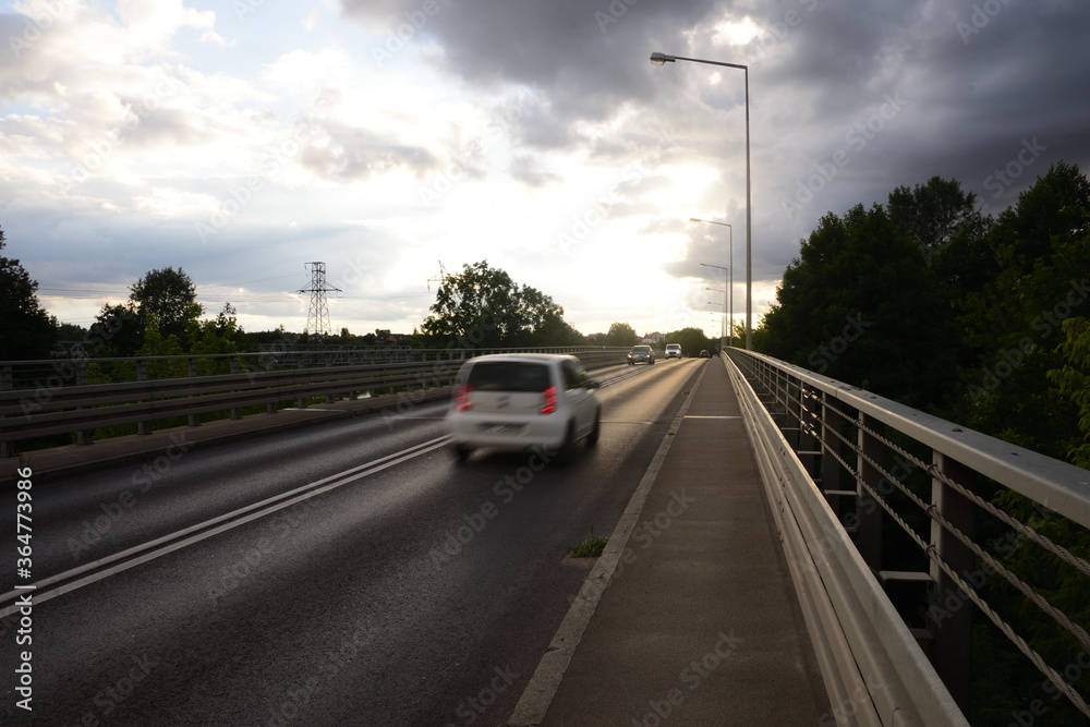 Blurry silhouettes of cars on the bridge against the background of clouds in the blue sky.
