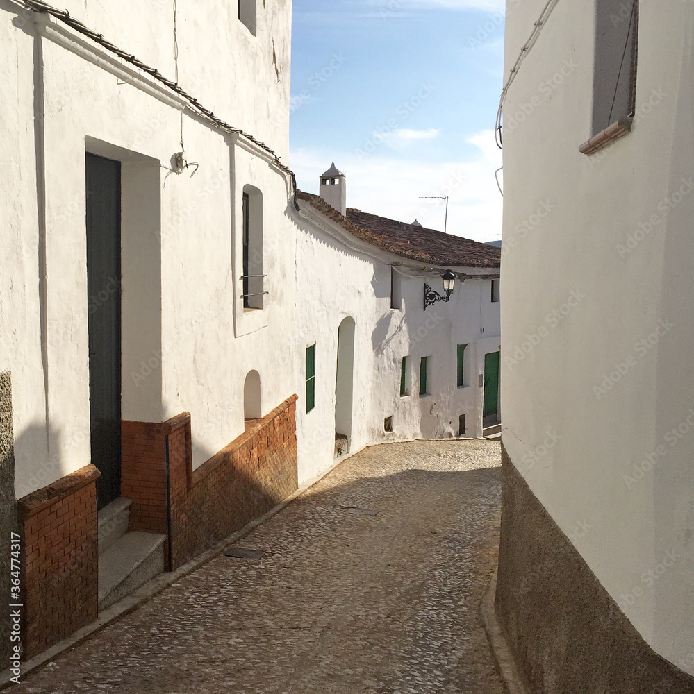Narrow street in the old town with white buildings. 
Spanish streets.