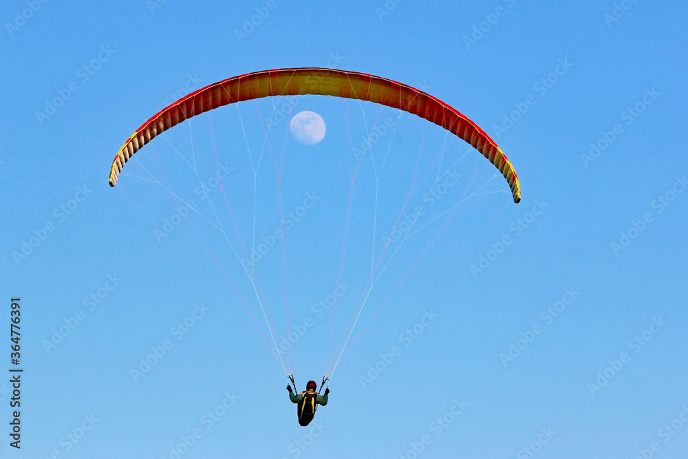 Paraglider flying wing in a blue sky with the moon Paraglider flying wing in a blue sky with the moon