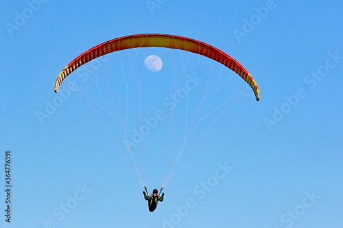 Paraglider flying wing in a blue sky with the moon 