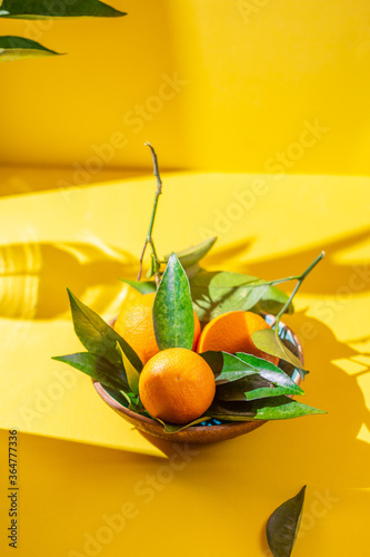 Whole oranges witl orange tree leaves on yellow background photo