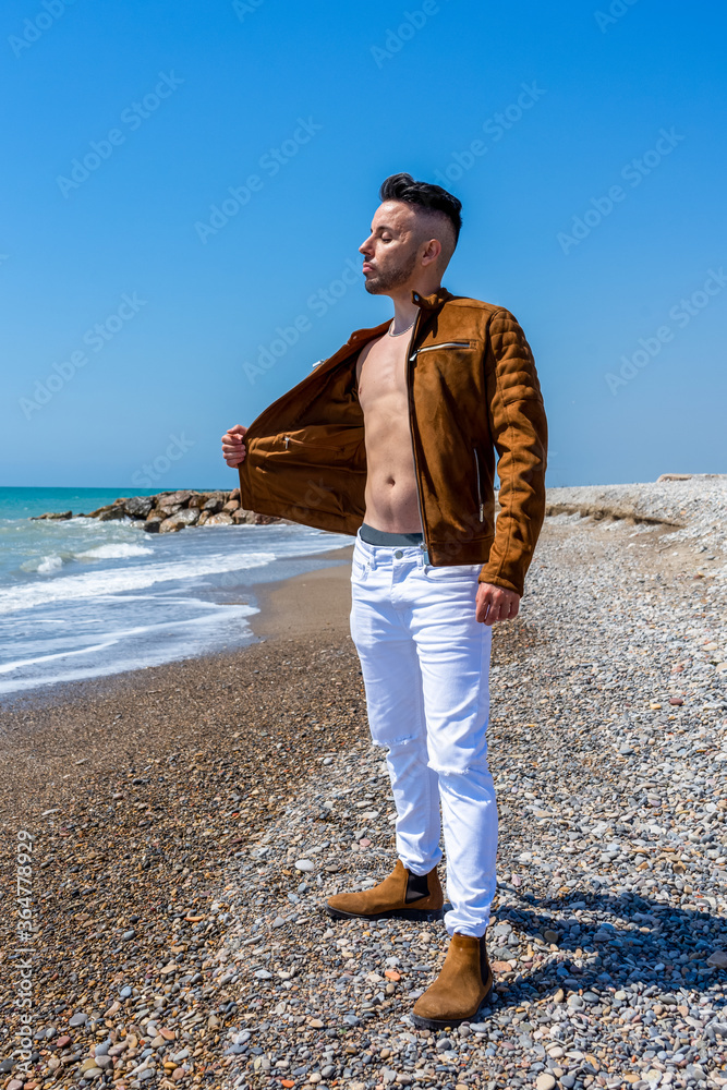 Young man in white pants and modern styling posing on the beach of the Mediterranean Sea in Burriana