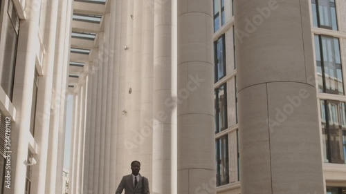 Lockdown of young African businessman wearing formalwear riding electrical kick scooter in the city center then stopping, looking around and continuing riding