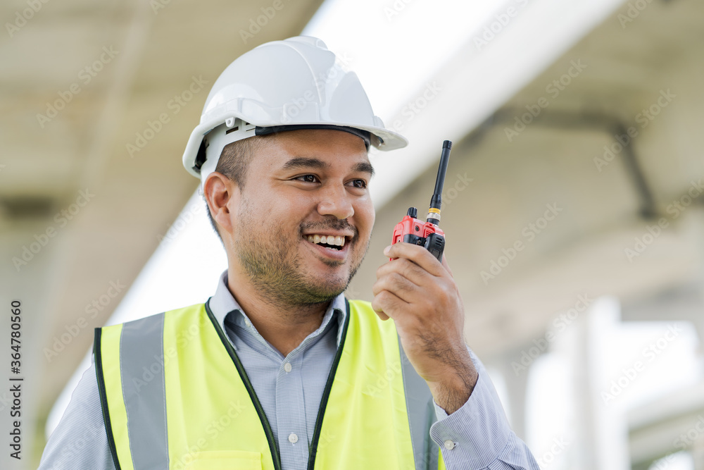 Portrait engineer handsome man or architect looking construction with the command of a radio. and white safety helmet in construction site. Portrait engineer handsome man or architect looking construction with the command of a radio. and white safety helmet in construction site.